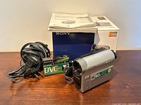 Sony camcorder with Carl Zeiss lens, showing front and side view with labels of 40x optical zoom and other features.