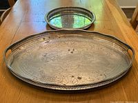 Pair of vintage silver plated serving trays displayed on a wooden table, showing overall condition and size difference.