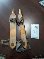 Pair of antique wooden ice skates with leather straps laid flat on a table, showing the top and side view.