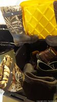 Full view of both camo Muck boots in bin with other footwear and yellow container in background.