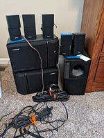 Group photo showing 5 small Bose speakers, 1 large subwoofer, 2 larger speakers, and connection cables arranged on carpet.