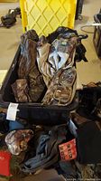 Camouflage clothing and bags displayed in an open black case with a yellow lid, showing multiple fabric items including vests and hats.