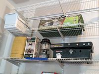 Shelving view showing green Coleman Ridgeview 8-person tent bag and black Coleman propane stove with lantern nearby.