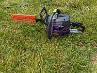 Side view of the purple and black Poulan Wild Thing chainsaw with an orange STIHL bar cover laying on grass.