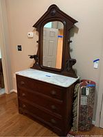 Front left side view of the three drawer wooden chest with white marble top and detached mirror leaning against the wall. Wooden drawer pulls visible, marble top intact.