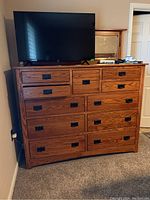 Front view of wooden chest with eleven drawers, attached mirror, and a TV on top.