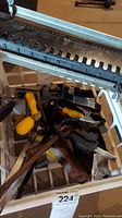 Photo showing assortment of metal clamps with yellow and black handles inside a container.