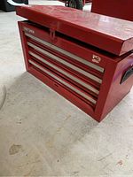 Front angle view of red Craftsman tool chest closed, showing four drawers and top pop lid lowering with latch, placed on concrete floor.