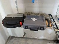 Two tool cases and Stanley levels on shelf: black case with red latches, gray Dremel case, and three Stanley spirit levels