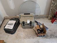 Smokeless smooth black grill, Camp Zero cooler, large round grill rack, box of starter logs and grill basket shown on floor.