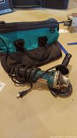 Makita angle grinder with cord and carrying bag on table, showing overall lot contents