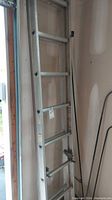 Full view of the aluminum extension ladder leaned against a wall in a garage, showing the rungs and side rails.