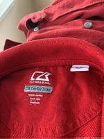 Close-up of red Cutter & Buck jacket label showing CB DryTec Luxe fabric and size XL
