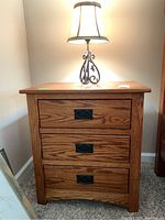 Front view of the oak nightstand showing three drawers and black metal handles with minor top surface marks.