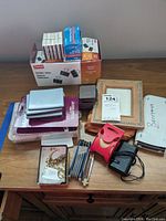 Lot overview showing binder clips, calculator, tape dispenser, frames, tools, and other items on wooden table