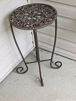 Full view of metal plant stand showing round, decorative top and three curled legs.
