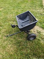 Side angle of the entire spreader shows the black plastic hopper attached to a metal frame with two black pneumatic tires.