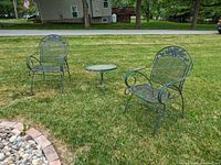 Two matching metal mesh chairs with floral backs and a small round metal side table set on grass.