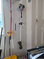 Full view of the Echo gas string trimmer hanging on the wall along with a yellow snow shovel