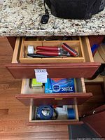 Photo showing three wooden drawers: top drawer with utensils, middle drawer with kitchen wraps and tape rolls, bottom drawer with miscellaneous items and tape