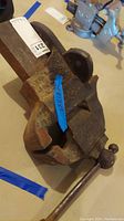 Top and angled view of a large rusted metal vise showing the jaw opening and handle, with blue tape showing measurements and identifying number.