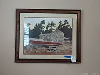 Framed print hanging on wall showing a red boat and stone house background