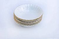 Stack of six white porcelain dessert bowls with scalloped edges and gold trim