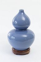 Front view of blue glazed double gourd vase on wooden stand with a white rim at the top opening.