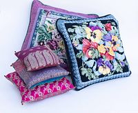 Five handmade vintage needlepoint pillows and small sari silk pillows arranged on white background.