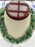 Front view of triple-strand jadeite bead necklace on display form showing size and bead texture.