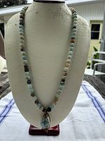 Full view of the beaded necklace with pendant displayed on a white bust stand, showing the length and bead color variation.