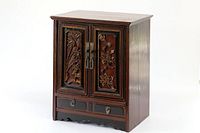 Front view of the antique miniature Chinese cabinet showing carved wooden doors with nature-themed panels and two drawers below the doors.