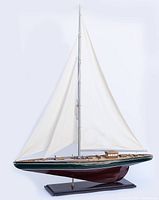 Full side view of the assembled wooden model sailboat with white sails, resting on black wooden stand.