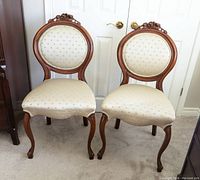 Pair of vintage balloon back chairs side by side, front view showing carved wood tops and pale green floral upholstery