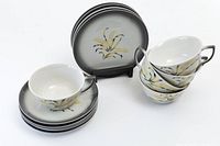 5 cups stacked next to 5 matching saucers and 5 cake plates arranged in a standing display, all showing the floral hand stencilled retro design.