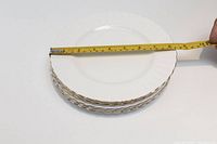 Stack of six white salad plates with gold rims and fluted edges measured and shown from side angle.