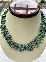 Front view of a multi-strand turquoise bead necklace displayed on a cream bust stand highlighting five strands of irregular turquoise beads knotted on dark cords.
