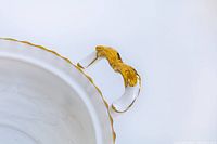 Close-up image of one ornate handle detailing gold paint and shape on white porcelain vegetable dish.