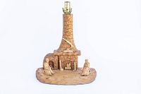 Front view of hand carved wooden lamp showing fireplace with two human figures, lamp fitting on top.