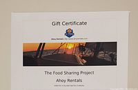 Paper gift certificate from Ahoy Rentals valid for a Sunset Sail for 2 adults with sunset boat image, promoting The Food Sharing Project.