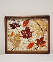Wooden framed rectangular tray with mosaic fall leaves design in red, orange, beige, and brown squares on a white square-tiled background.