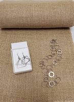 Photo shows a silver-tone necklace made of connected circular rings and a pair of triangular shaped pierced earrings on a textured brown fabric background.