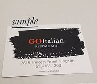 Photo of a white gift card with black brush stroke design and GO Italian Restaurant branding including address and contact details.