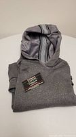 Folded view of grey hoodie with visible striped lining inside hood and business card on top.