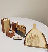 Photo showing 3 wood tea light holders, 4 wood coasters, and 1 live edge charcuterie board arranged on white table.