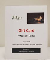 Photo of a white gift card with text detailing a 1 hour massage valued at $110 donated by Integro Health & Wellness. The card includes a small photo of lit candles and rolled towels.