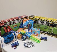 Photo showing boxed Ladder Toss and Bean Bag Toss game sets alongside Aqua Grip football, Aqua Monster Screamerz balls, Splash Ball set, inflatable beach ball, bubble wands, pet collar and bracelet, and fidget bracelets.