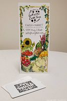 Photo shows a $50 Salt of the Earth Farm plastic gift card placed on a table next to a tall, colorful informational card with images of produce and farm details.