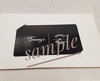 Photo shows a black rectangular gift card with Tommy's and Smoke 'N' Barrel branding, presented inside a white card holder.