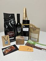 All items arranged on white surface including coffee, olive oil, tea, bath salts, soap, necklace, and gift cards